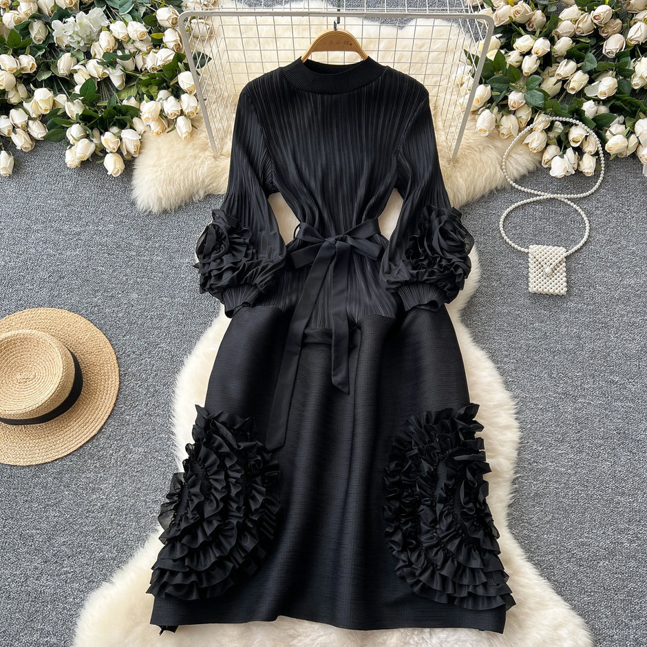 Black dress with ruffled sleeves and bottom on a hanger against a decorative background with flowers and a hat.