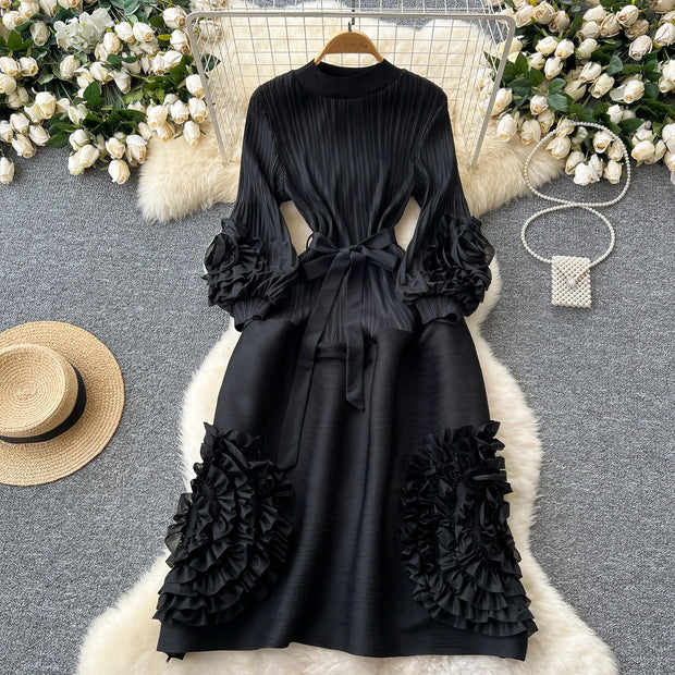 Black dress with ruffled sleeves and bottom on a hanger against a decorative background with flowers and a hat.