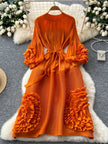 Orange dress with ruffled sleeves and bottom on a hanger against a decorative background.