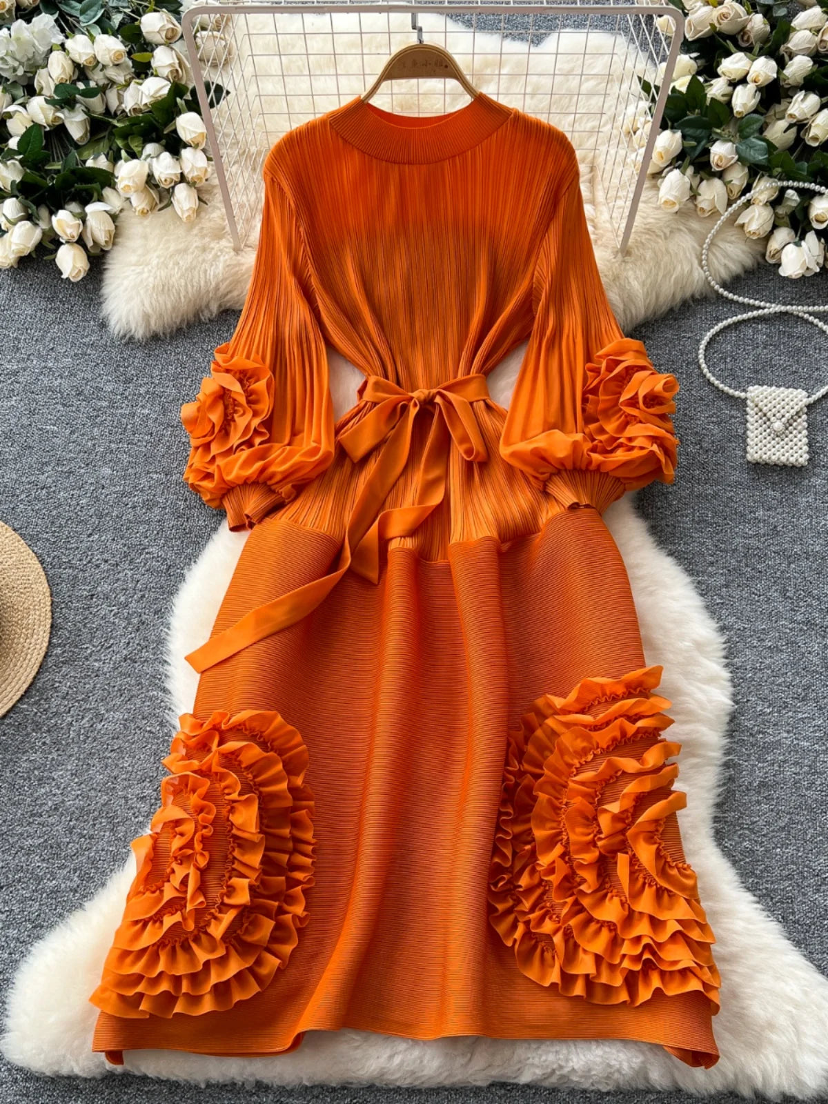 Orange dress with ruffled sleeves and bottom on a hanger against a decorative background.