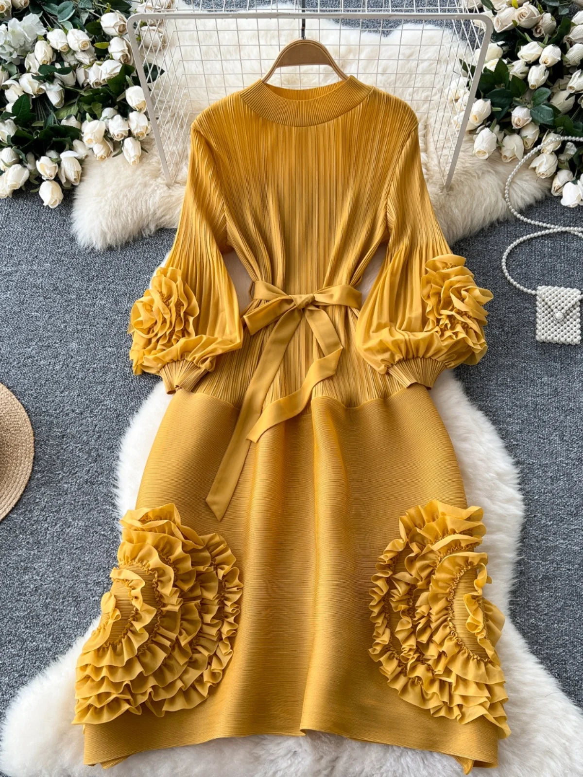 Yellow dress with ruffled sleeves and bottom on a hanger against a decorative background.