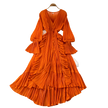 Orange pleated dress on a hanger with decorative items on a gray surface