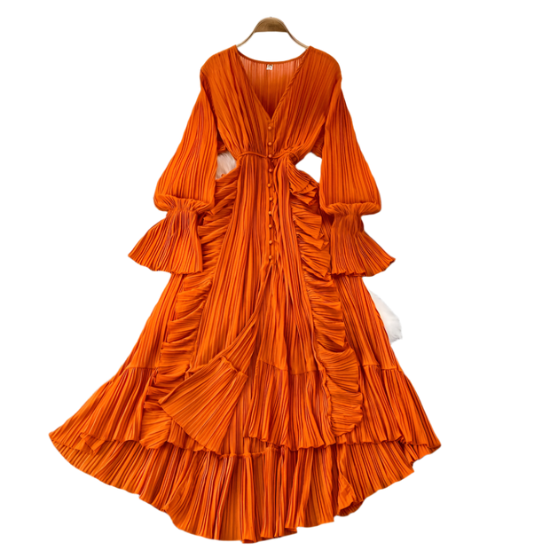 Orange pleated dress on a hanger with decorative items on a gray surface