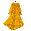 Yellow pleated dress on a hanger with decorative items on a gray surface.