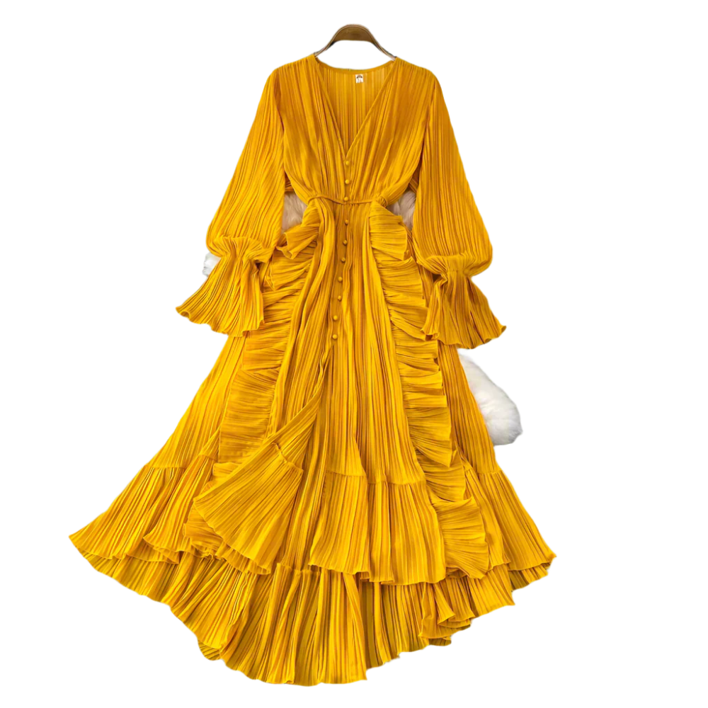 Yellow pleated dress on a hanger with decorative items on a gray surface.