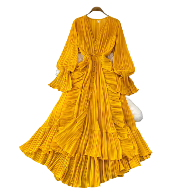 Yellow pleated dress on a hanger with decorative items on a gray surface.